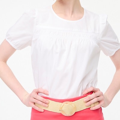 A woman wearing a white puff-sleeve top, tan belt, and coral skirt